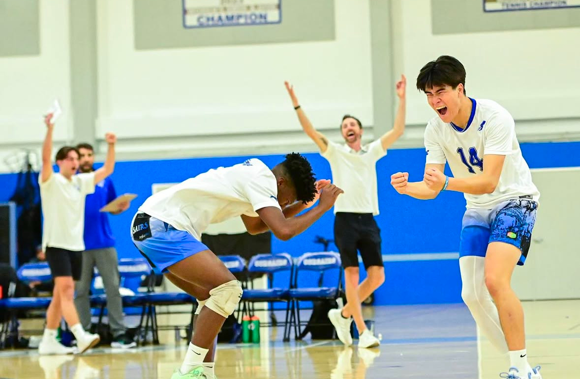 Two players are celebrating by pumping their fists with the coaches and teammates celebrating in the background with their hands in the air.